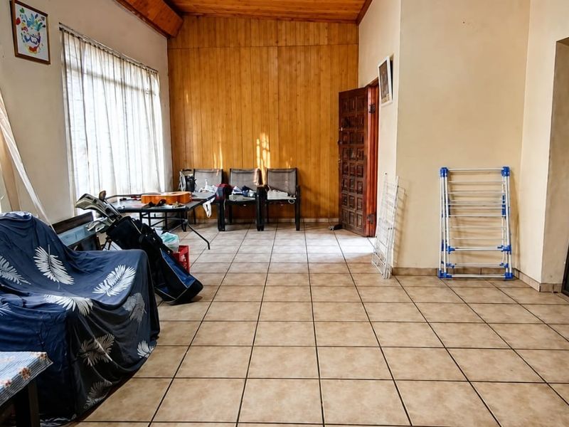 Spacious living area featuring tiled flooring, timber wall paneling, and exposed ceiling beams, offering a versatile layout with abundant natural light.