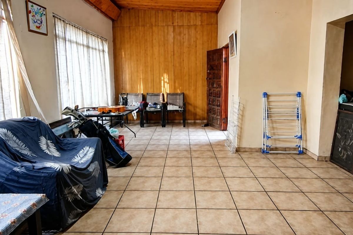 Spacious living area featuring tiled flooring, timber wall paneling, and exposed ceiling beams, offering a versatile layout with abundant natural light.