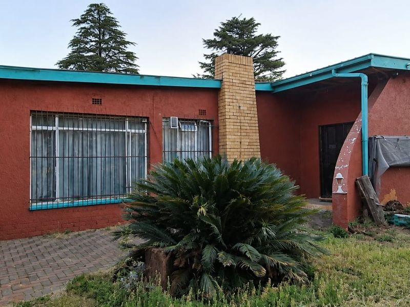 Rear exterior view of the house featuring a brick chimney, paved patio area, and security bars on windows.