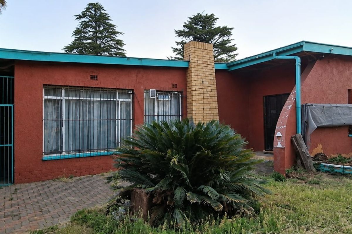 Rear exterior view of the house featuring a brick chimney, paved patio area, and security bars on windows.
