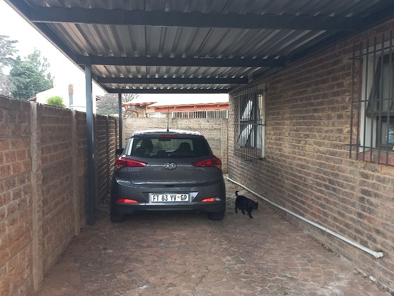 A covered carport area featuring a corrugated metal roof, brick boundary walls, and paved flooring, providing secure off-street parking.