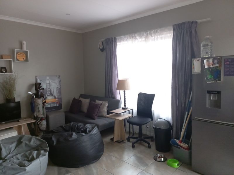A living area featuring tiled flooring and large window with curtain rails, providing a functional space for relaxation.