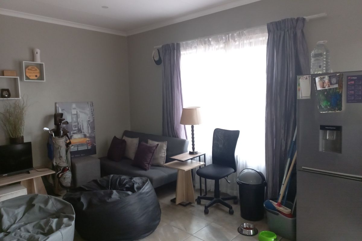 A living area featuring tiled flooring and large window with curtain rails, providing a functional space for relaxation.