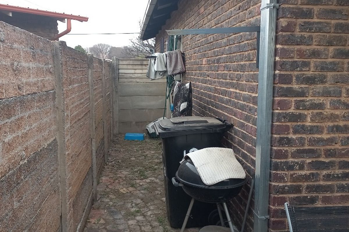 A narrow rear exterior side passage featuring brick walling, a metal downpipe, and paved ground surface.