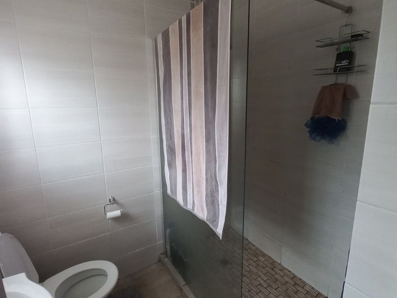 A functional bathroom featuring a walk-in shower with a glass screen, a pedestal basin, and a toilet, finished with neutral wall and floor tiles.
