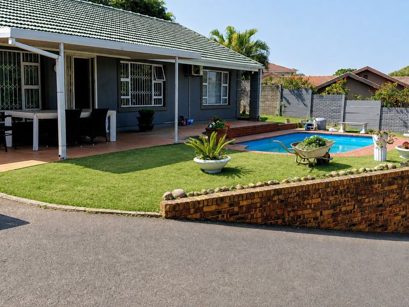 Rear exterior view featuring a covered patio, swimming pool, landscaped lawn, and brick retaining wall.