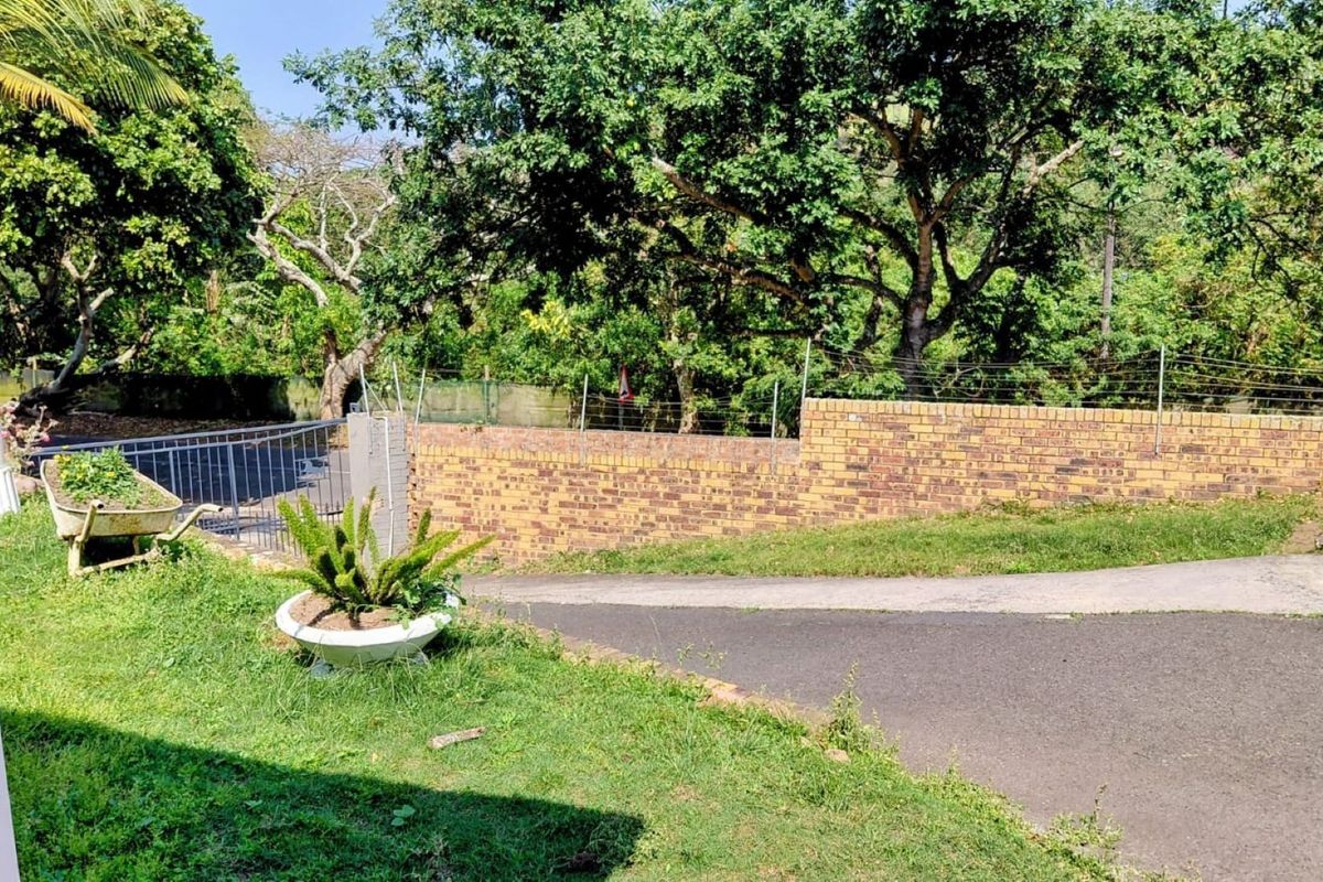 A view of the rear garden area featuring a brick boundary wall with electric fencing and an asphalt driveway.