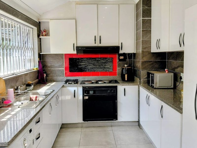 A functional kitchen featuring white cabinetry, granite countertops, a built-in oven with gas hob, and a tiled splashback with a window security gate.