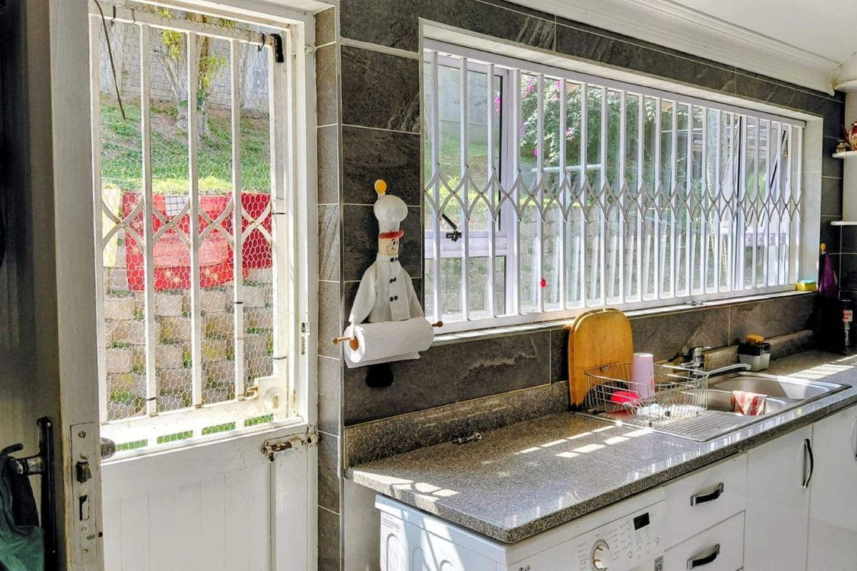 A functional kitchen featuring granite countertops, tiled walls, and built-in cabinetry, with security gates installed on the windows and exterior door.