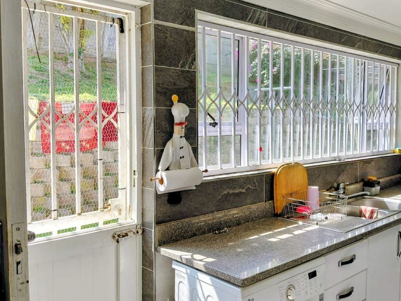 A functional kitchen featuring granite countertops, tiled walls, and built-in cabinetry, with security gates installed on the windows and exterior door.