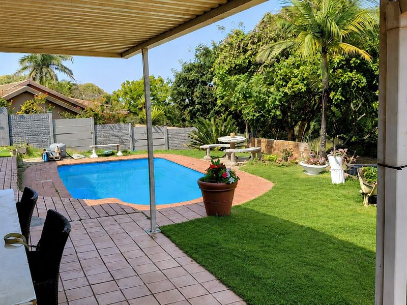 Outdoor entertainment area featuring a swimming pool, covered patio with tiled flooring, and a landscaped garden with established trees and boundary walling.
