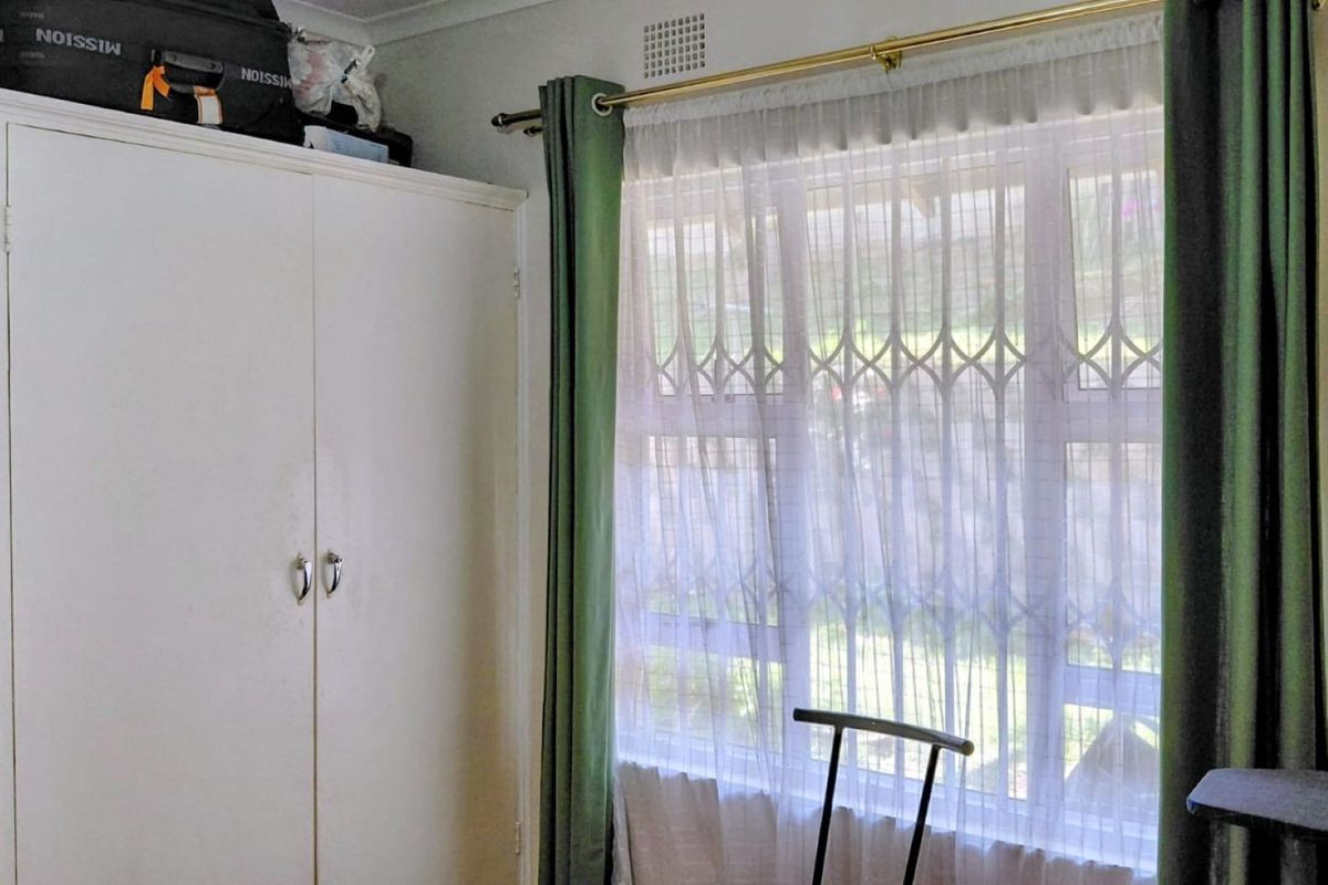 A bedroom featuring a built-in wardrobe and a window fitted with a security gate and curtain rod.