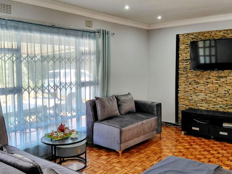 A comfortable living room featuring warm parquet flooring, a textured stone feature wall, and large sliding doors providing natural light.