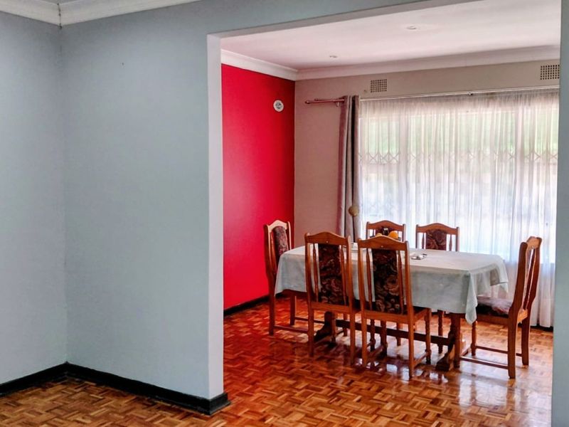 Dining room featuring classic parquet flooring, a bold red accent wall, and a stone feature wall, creating a distinct and defined living space.