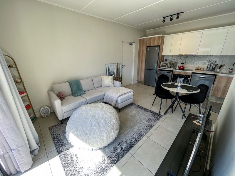 Modern open-plan living area featuring a contemporary kitchen with sleek cabinetry, integrated appliances, and tiled flooring throughout the combined lounge and dining space.