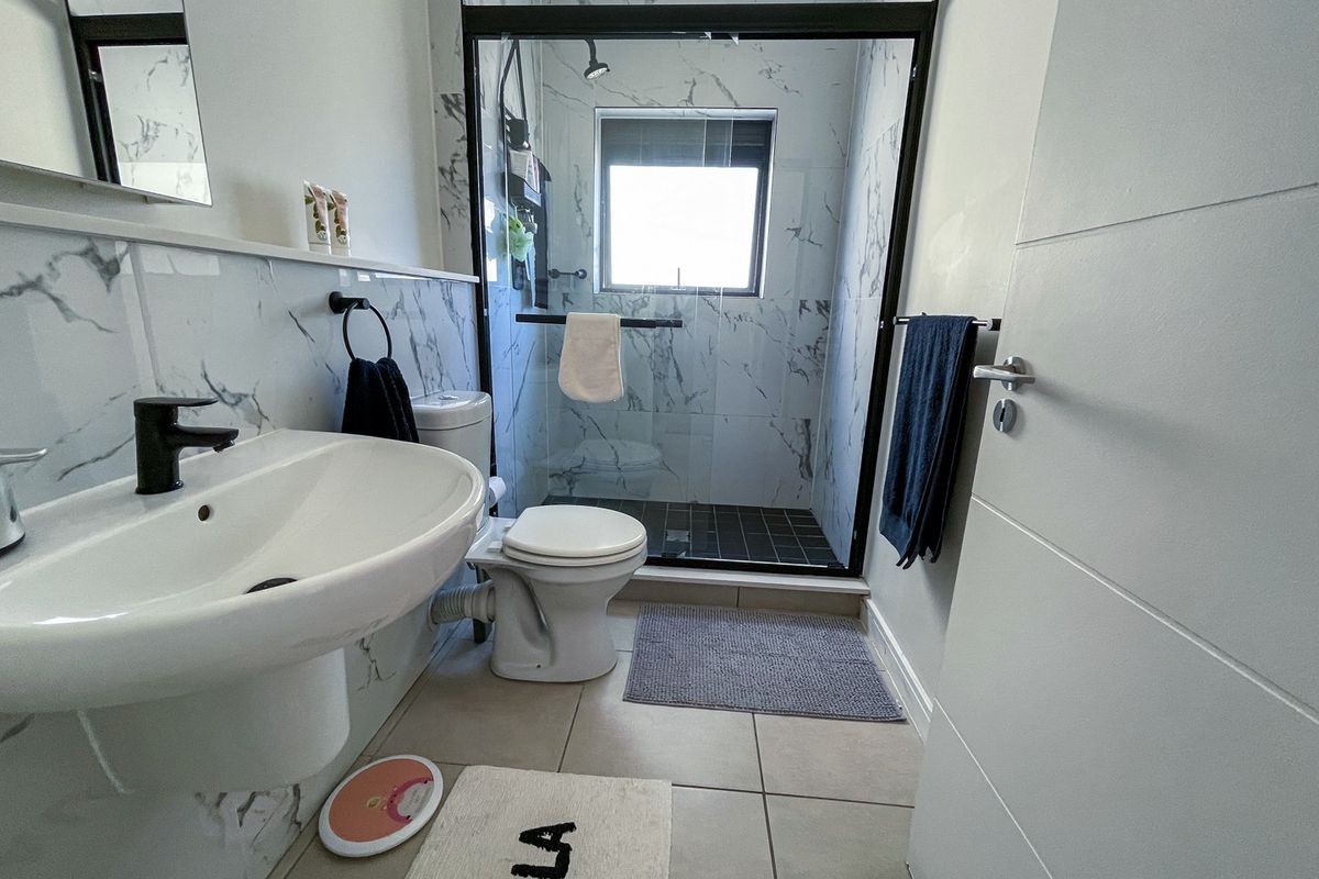 Modern bathroom featuring marble-look wall tiles, a pedestal basin with a black mixer tap, and a walk-in shower with a glass screen.