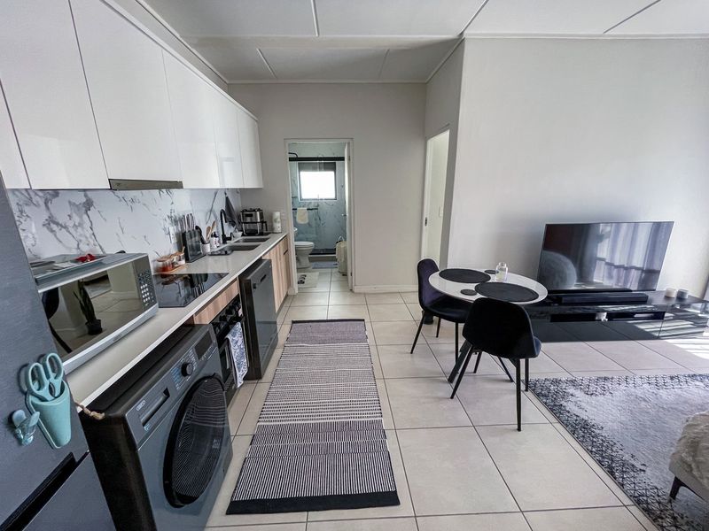 Modern open-plan kitchen and living area featuring sleek white cabinetry, marble-look splashback, and tiled flooring, with direct access to an adjacent bathroom.