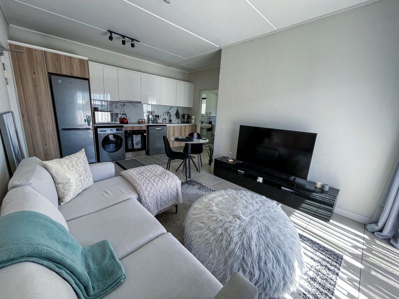 Modern open-plan living area featuring a contemporary kitchen with built-in cabinetry, integrated appliances, and tiled flooring, seamlessly flowing into the lounge space.