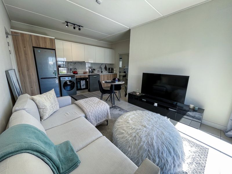 Modern open-plan living area featuring a contemporary kitchen with built-in cabinetry, integrated appliances, and tiled flooring, seamlessly flowing into the lounge space.