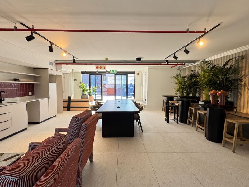 Spacious open-plan living and kitchen area featuring modern tiled floors, exposed industrial-style fire sprinkler piping, track lighting, and direct access to an outdoor patio.
