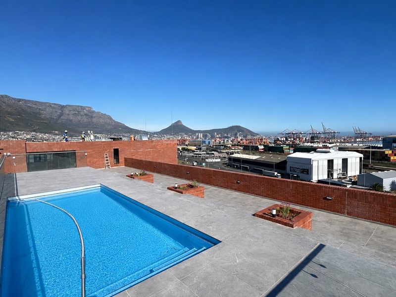 Rooftop terrace featuring a swimming pool with glass balustrades, brick perimeter walls, and panoramic mountain and city views.