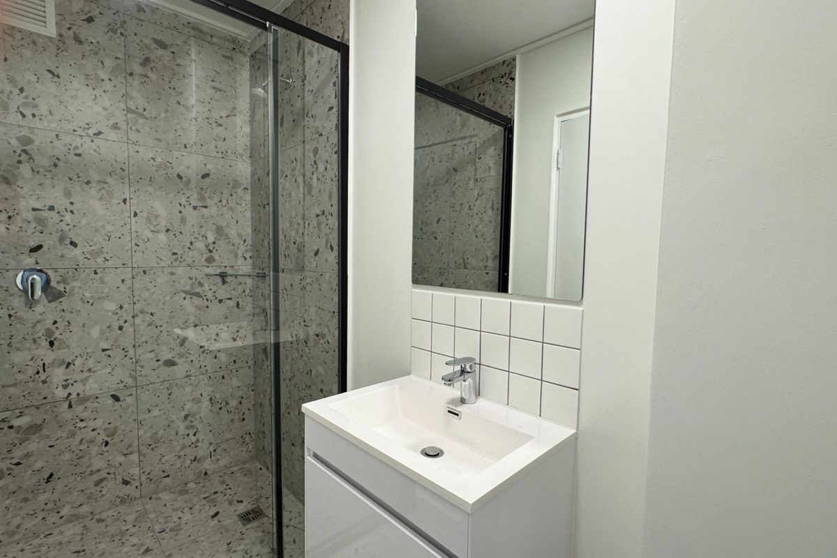 Modern bathroom featuring a glass-enclosed shower with terrazzo-style tiling, a sleek vanity basin, and a clean, contemporary aesthetic.
