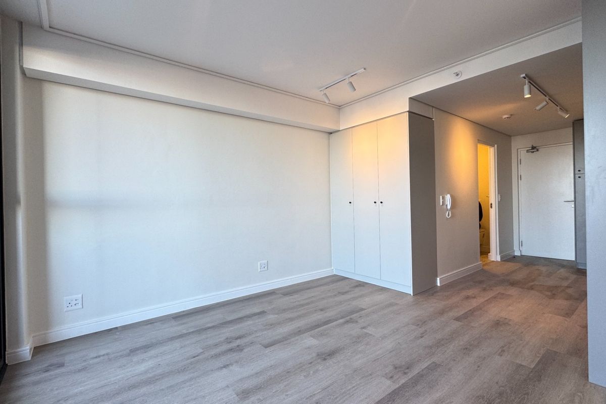 A bright, modern bedroom featuring neutral laminate flooring, built-in cupboards, and contemporary track lighting, offering a clean and versatile living space.