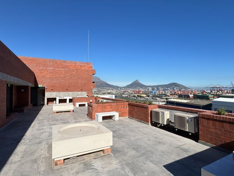 Spacious rooftop terrace featuring brick masonry, built-in concrete seating, and expansive panoramic views of the city and mountains.