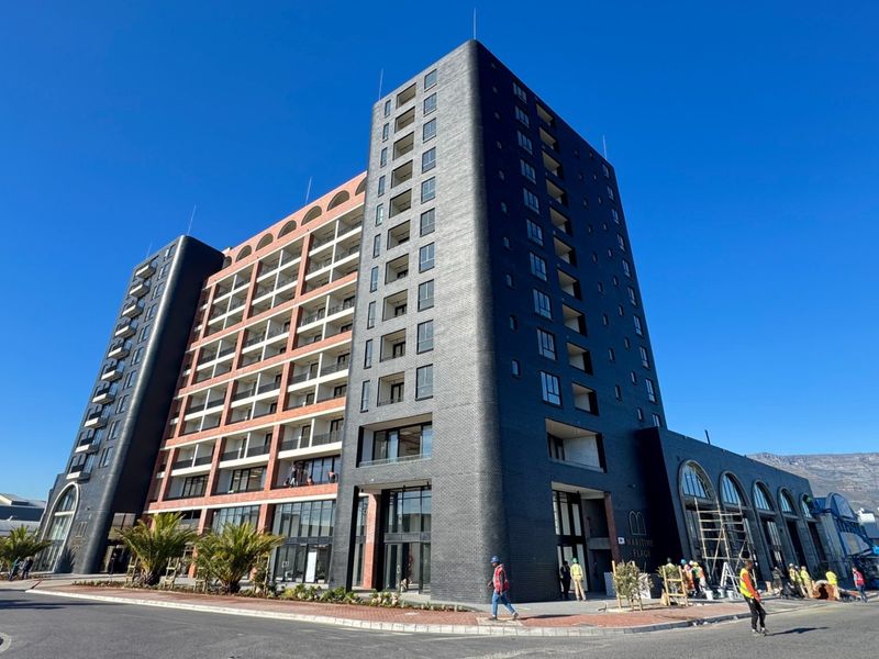 Modern multi-story apartment building featuring a striking dark brick facade, integrated balconies, and large windows in a prominent street-facing location.