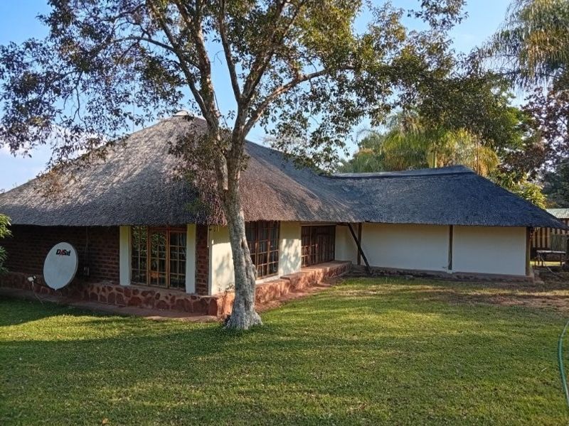 Rear view of a traditional farmhouse featuring a thatched roof, stone base detailing, and timber-framed windows set within a spacious garden.