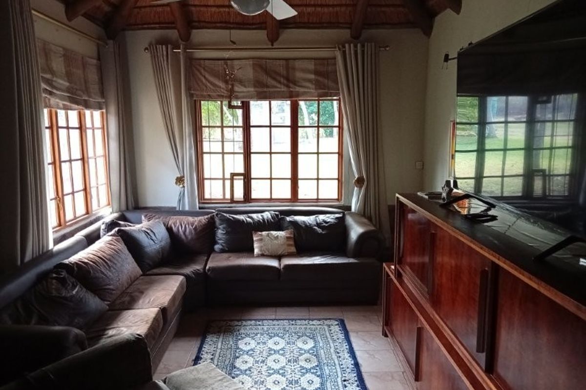 Cozy living room featuring a traditional thatched roof with exposed timber beams, tiled flooring, and large timber-framed windows overlooking the garden.