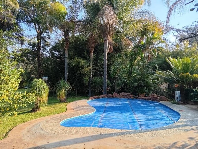 A private swimming pool area featuring a paved surround, natural stone rockery, and a blue pool cover, set within a lush garden landscape.