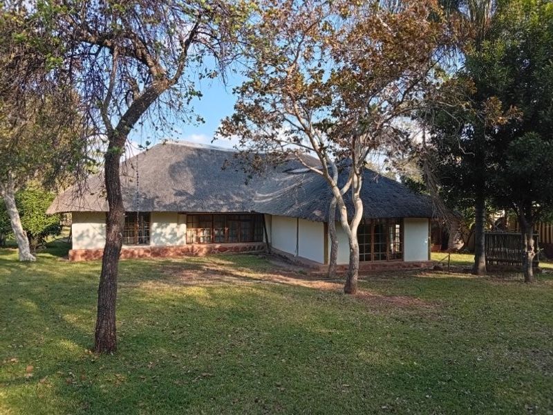Rear view of a traditional farm-style dwelling featuring a classic thatch roof, timber-framed windows, and a stone plinth set within a spacious garden.
