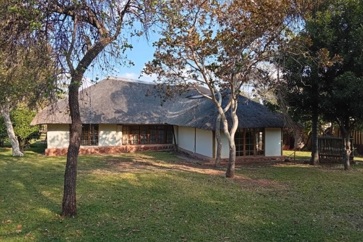 Rear view of a traditional farm-style dwelling featuring a classic thatch roof, timber-framed windows, and a stone plinth set within a spacious garden.