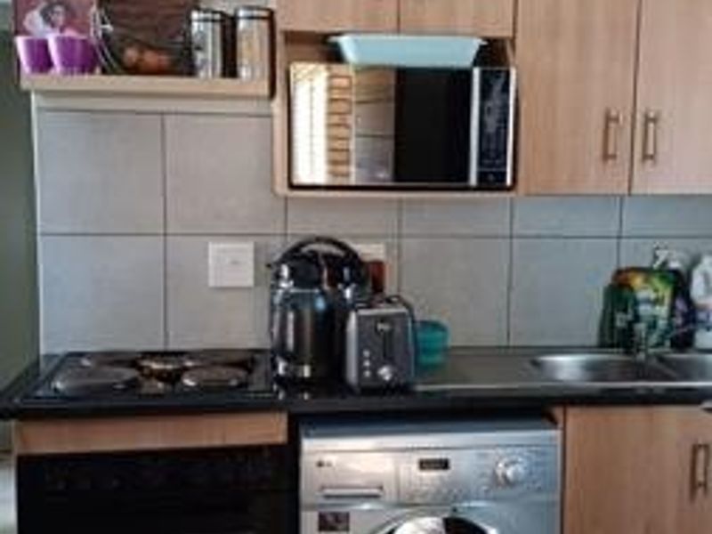 A functional kitchen featuring light wood-finish cabinetry, tiled backsplash, built-in oven, hob, and integrated microwave with tiled flooring.