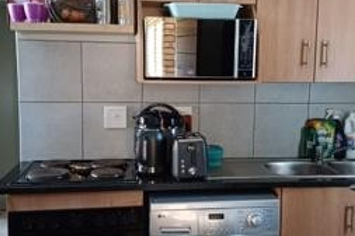 A functional kitchen featuring light wood-finish cabinetry, tiled backsplash, built-in oven, hob, and integrated microwave with tiled flooring.
