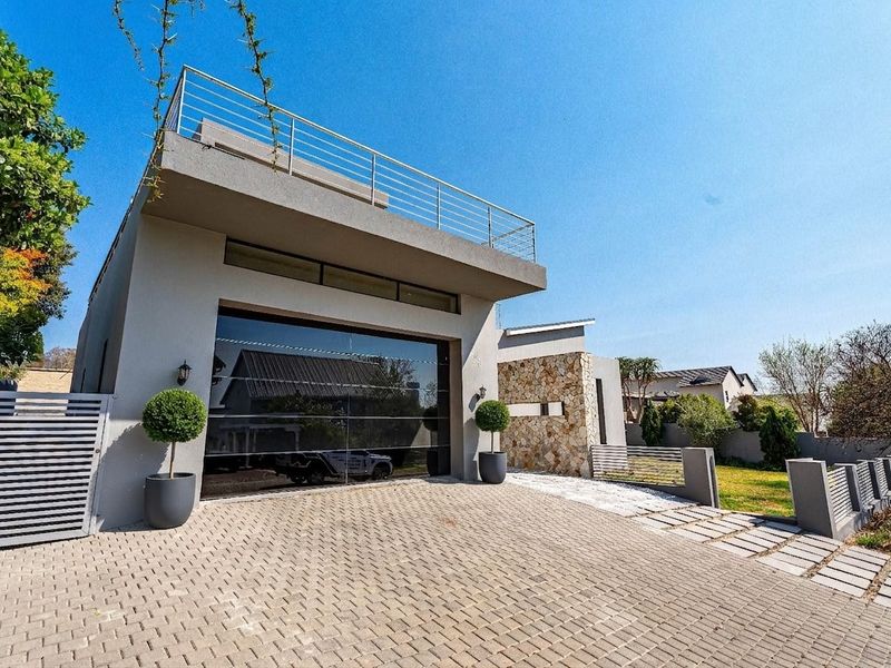 Modern front elevation featuring a paved driveway, stone-clad accents, a sleek garage door, and an upper-level balcony with metal railings.