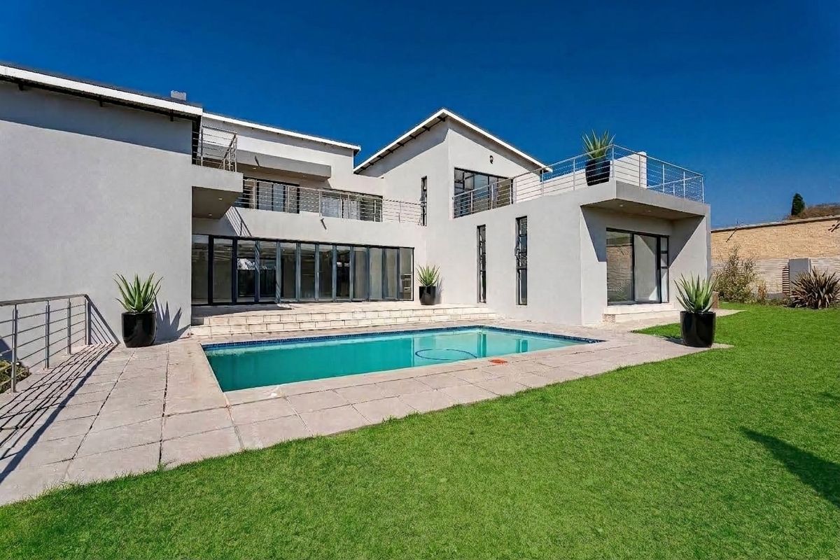 Modern double-story residence featuring a swimming pool, paved patio area, and upper-level balconies with stainless steel railings overlooking a well-maintained garden.