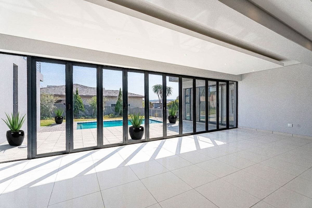 Spacious, modern living area featuring large format floor tiles, recessed ceiling lighting, and expansive aluminium stacker doors opening to a pool area.