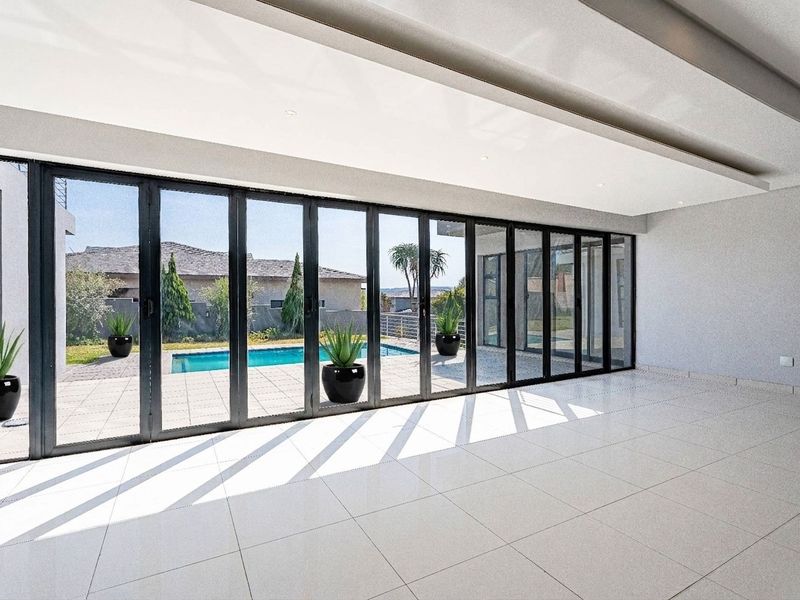 Spacious, modern living area featuring large format floor tiles, recessed ceiling lighting, and expansive aluminium stacker doors opening to a pool area.