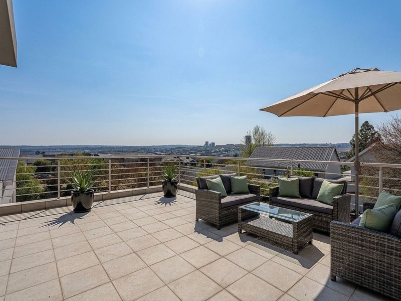 Spacious elevated balcony featuring tiled flooring and a stainless steel balustrade, offering expansive panoramic views of the surrounding area.