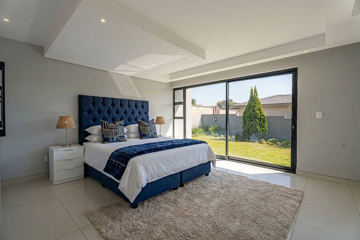 Spacious bedroom featuring modern tiled flooring, recessed ceiling with downlights, and large sliding glass doors providing direct access to the garden.