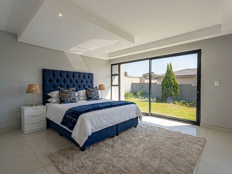Spacious bedroom featuring modern tiled flooring, recessed ceiling with downlights, and large sliding glass doors providing direct access to the garden.