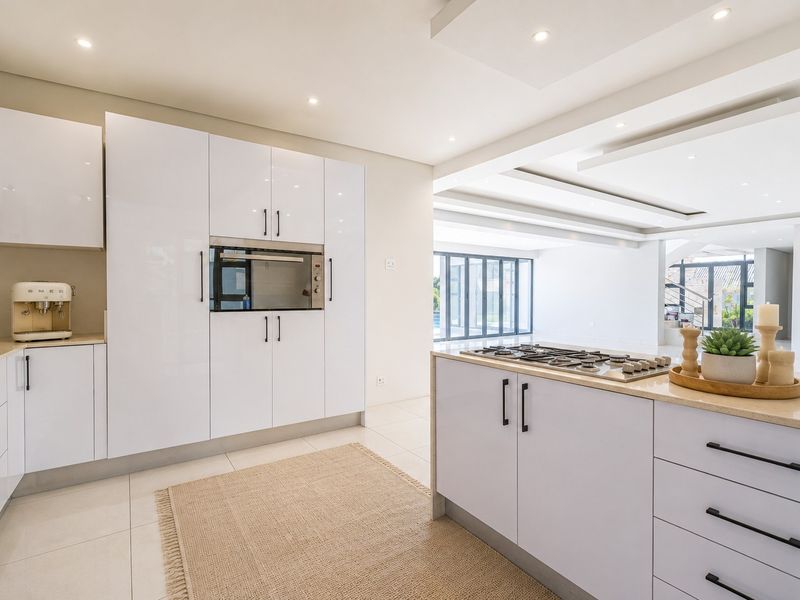 Modern kitchen featuring high-gloss white cabinetry, a central island with a gas cooktop, stone countertops, and integrated appliances in an open-plan layout.