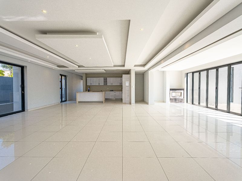 Spacious open-plan living area featuring a modern kitchen, tiled floors, recessed ceiling details, a built-in fireplace, and large sliding doors leading to the exterior.