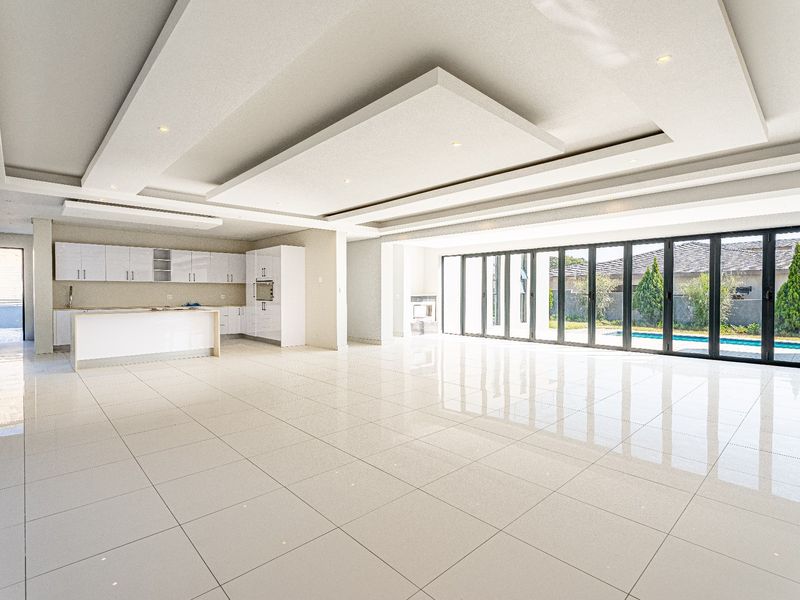 Spacious open-plan living and kitchen area featuring high-gloss tiled floors, modern cabinetry, recessed ceiling details, and large bi-fold doors opening to the pool area.