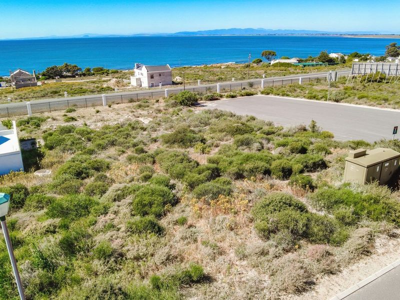 Aerial view of a vacant residential plot featuring native vegetation, adjacent paved road, and coastal ocean views.