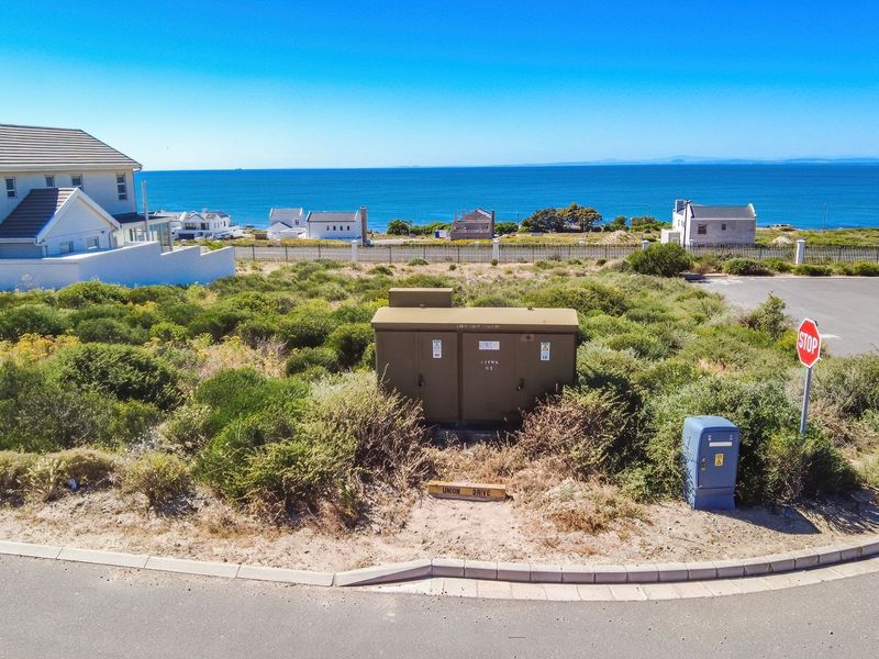 Aerial view of a vacant residential plot featuring coastal views, local infrastructure, and proximity to the ocean.