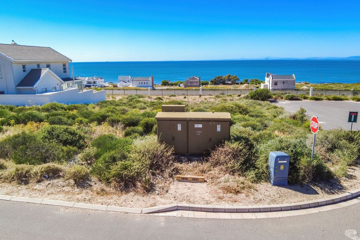 Aerial view of a vacant residential plot featuring coastal views, local infrastructure, and proximity to the ocean.