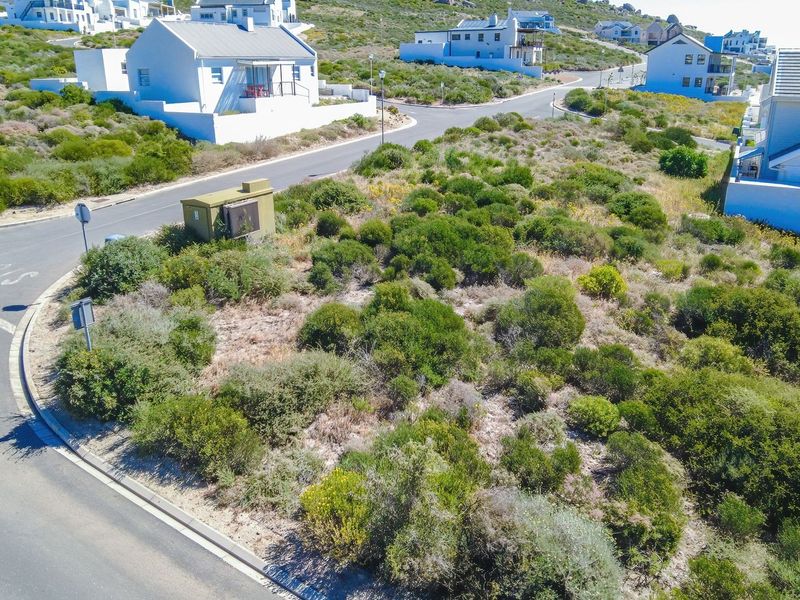 An aerial view of a vacant residential plot situated on a corner lot, featuring native coastal vegetation and adjacent paved street access.